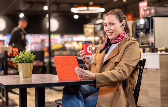 Woman excitedly looking at her tablet in a Circle K café while drinking a hot drink