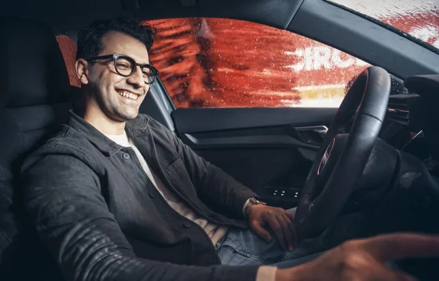 Man smiling in his car while it's being washed